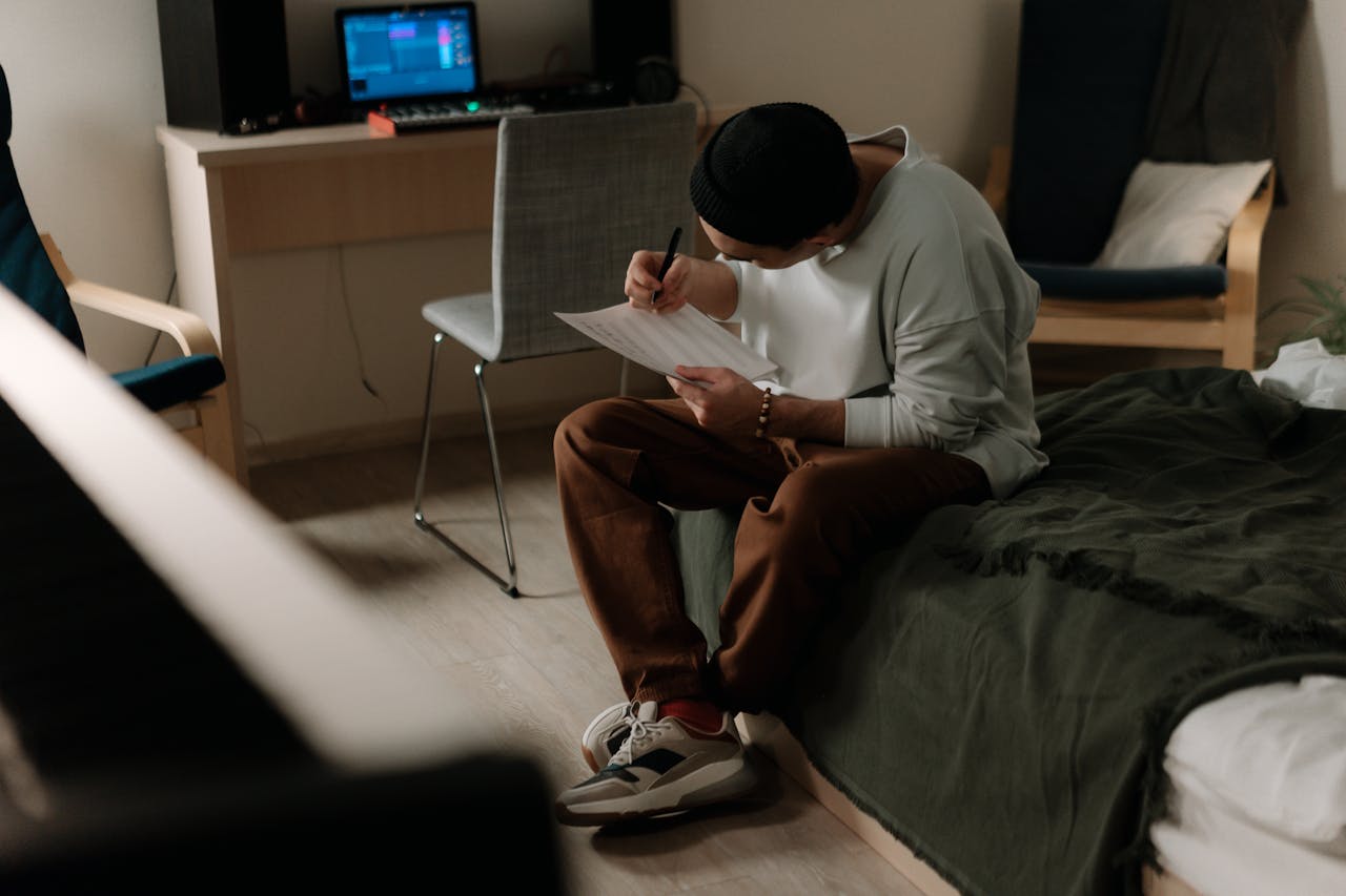 A man sits in a cozy home studio, focused on songwriting and composing music.